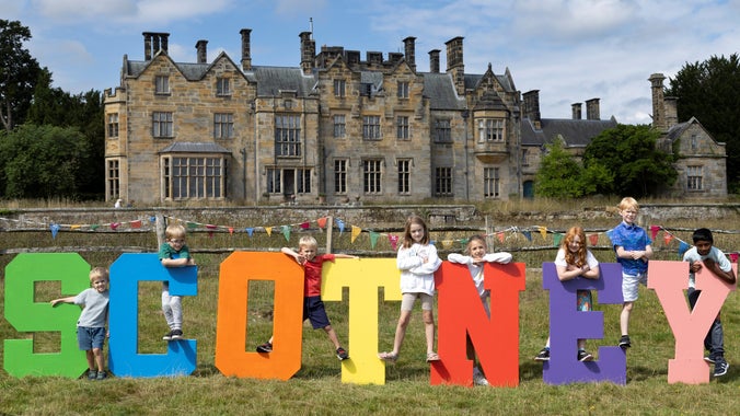 Eight children posing on the colourful SCOTNEY letter at the Summer of Play event at Scotney Castle, Kent